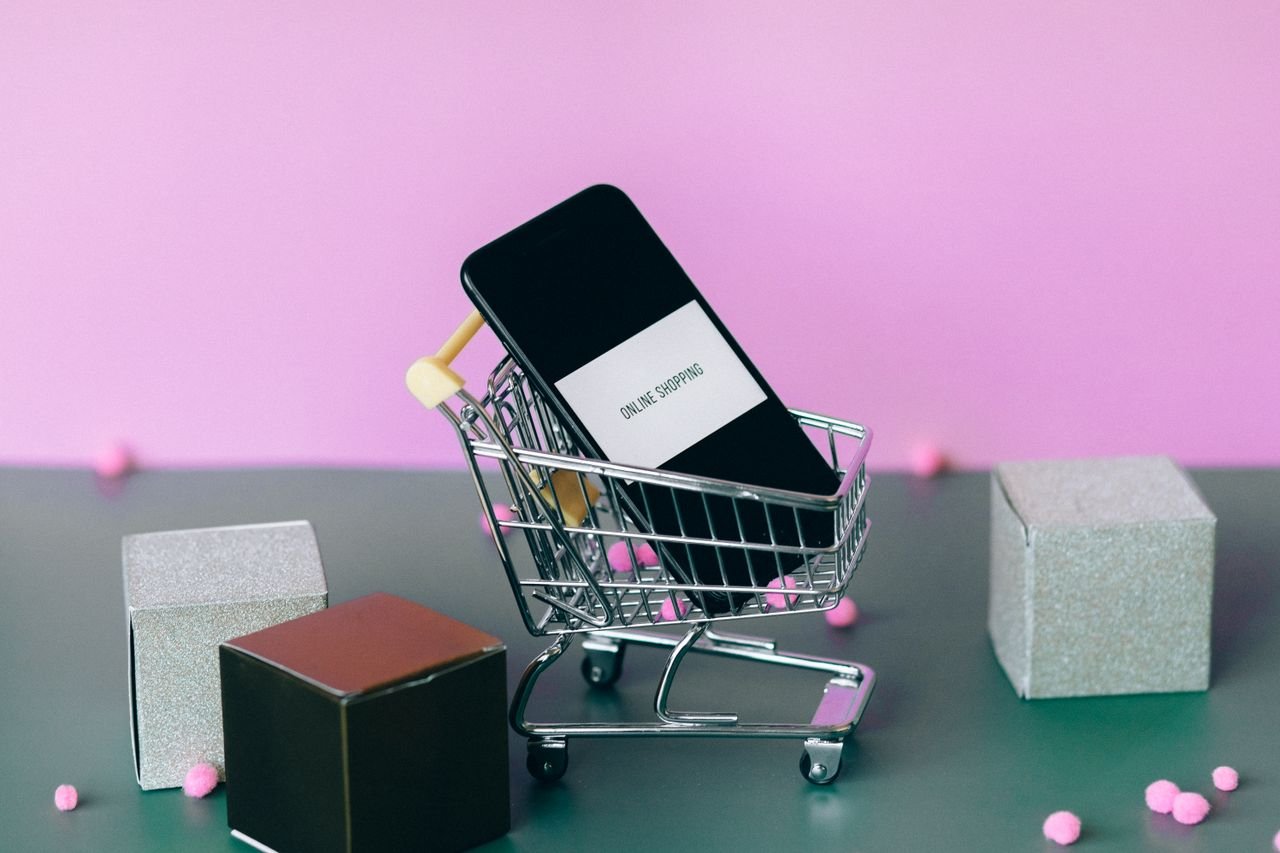Services A smartphone with a shopping cart depicting the concept of online shopping in a colorful studio setup.