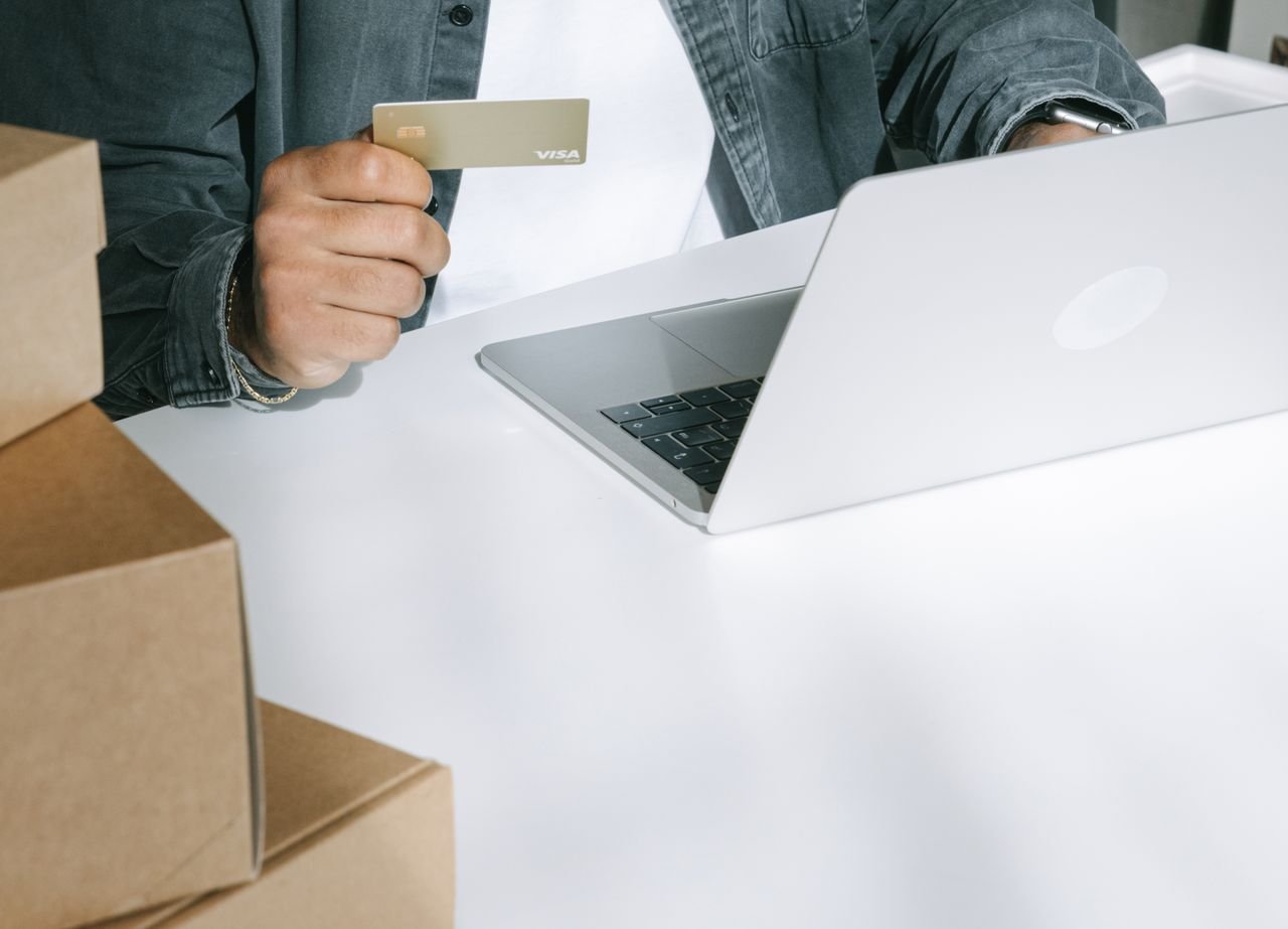 Mastering the First Impression: Your intriguing post title goes here Person using a credit card for online shopping on a laptop surrounded by shipping boxes.